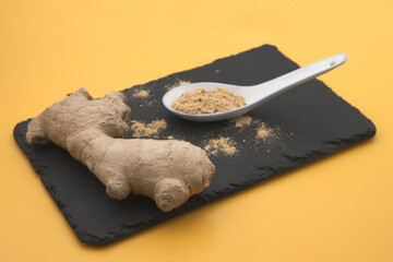 A ginger root next to a teaspoon of powdered ginger