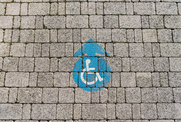 Fototapeta na wymiar Handicapped wheelchair sign on a sidewalk, blue color on grey bricks, round-shaped, with arrow. 