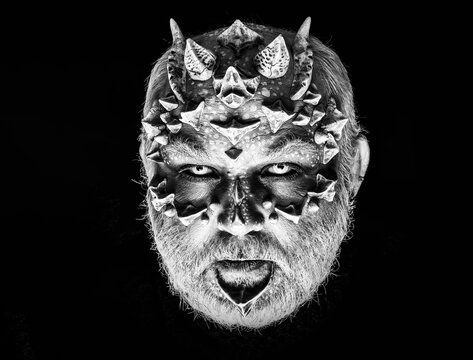 Demon head on black background. Alien or reptilian makeup. Monster with sharp thorns and warts on face. Man with dragon skin and grey beard. Horror and fantasy concept.