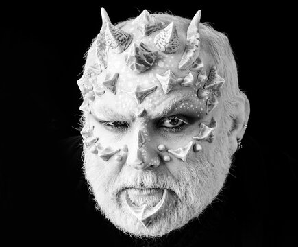 Devil with frowning face and white eyes. Evil with dragon skin and beard. Alien or reptilian makeup with thorns and warts. Demon head on black background. Horror and fantasy concept.