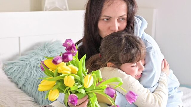 Affectionate loving hugs of daughter and mom on mother's day. A little girl gives a bouquet of yellow and purple tulips to her mother. Gift for March 8 for mommy. FullHD footage. slow-motion 