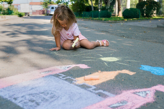Girl drawing castle with colored chalks on the sidewalk near the house on sunny summer day. Kids painting outside. Creative development of children.