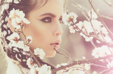 Spring girl and flowers. Pretty woman with flower blooming, fashionable makeup on face, outdoor, natural background.