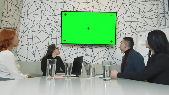A team of business people in a conference room watching a picture on a TV screen. Chrome quay on the screen and trekking points. Mobile camera Business business people during a video conference