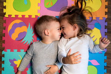 childhood, family friendship, games - close up portrait Two funny joy happy smiling little toddler peschool kids siblings twins brother with sister have fun lie playing on puzzles mat at home indoors