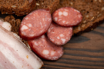 Sandwich with smoked brisket sliced on grain bread and homemade sausage on a wooden cutting board.