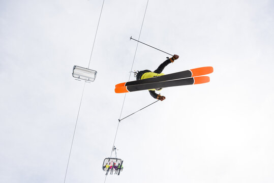 Over the head view of male skier jumping in midair with ski lift in the background
