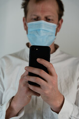 Portrait of a straight man with a white shirt with curly hair and a direct firm look and face mask to protect against covid19, he has a black mobile phone
