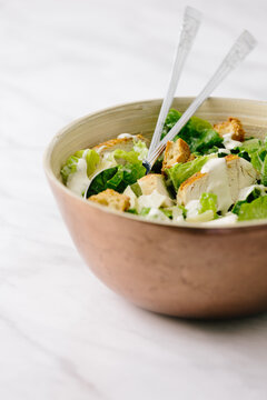 Copper bowl with chicken caesar salad with serving spoons