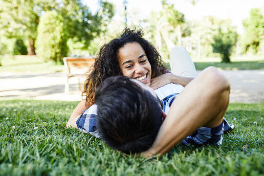Smiling girl lying over her boyfriend on lawn in park.