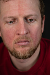 a close up portrait of a man in a red sweater and a disturbed facial expression and a desperate look
