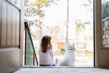 A girl and her dog sitting by an open door looking outside