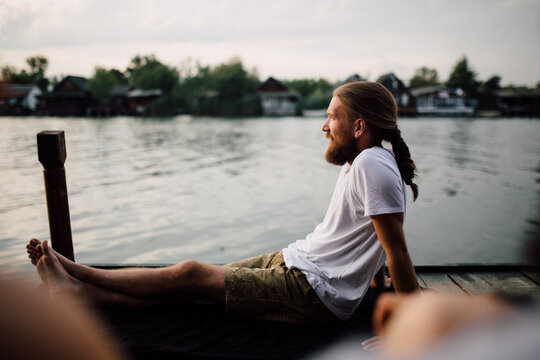 A Man With A Beard And Ponytail Sitting On A Dock
