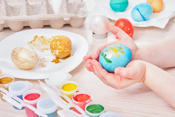 child paints egg for Easter on a wooden table,
