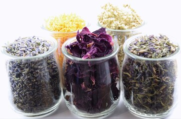 Glass jars with colorful dried herbal flowers on white background