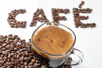 Transparent cup of coffee with a lot of crema and blurred cafe written with coffee beans in the background