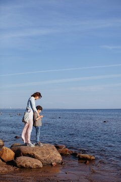Mother and son standing at rocks near the sea
