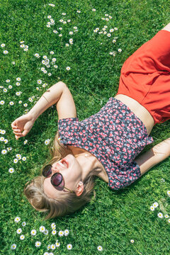 Cute girl with sun glasses laying on the grass with flowers.