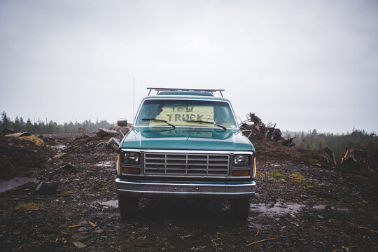 An old truck on the side of the road with a ""Tow Truck"" sign in the windshield