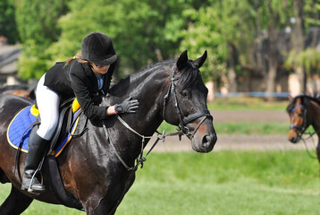 Young rider girl sitting on a black-brown horse stroking horses neck