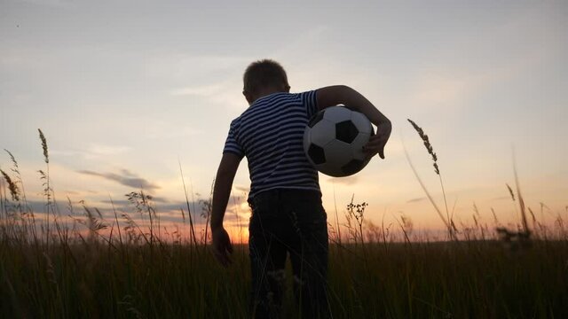Childhood dream. boy holding soccer ball walking in the park silhouette. happy family kid dream concept. kid boy walking on the field silhouette at sunset carries a soccer ball. fun baby winner