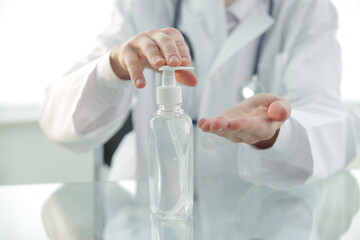 Doctor with a stethoscope in a protective mask in a clinic treats his hands with an antiseptic. Close-up