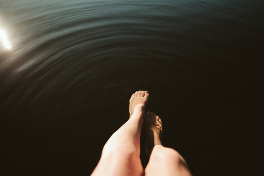 a young woman's feet dangle into the water of a lake