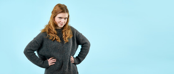 A young pretty girl in a knitted sweater shows emotions on a light blue background. A place to copy...