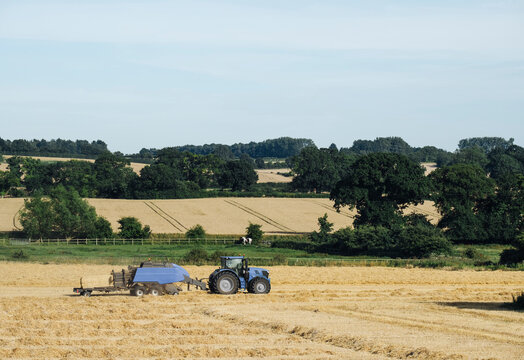 Tractor and baler, baling straw in a recently harvested field. N