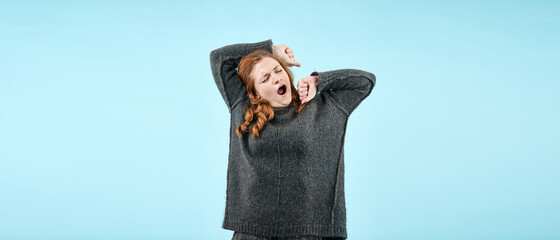 Portrait of a young girl in a sweater stretching and yawning with fatigue on camera on an isolated...