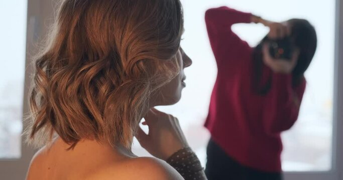 Blonde woman model and photographer. Female photographer takes pictures of the young blonde caucasian woman in studio. Clip has rack of focus