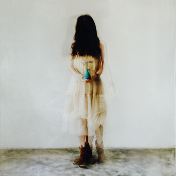 Movement shot of unrecognisable female, wearing flowing dress and pixie boots, holding a small vase of lavender