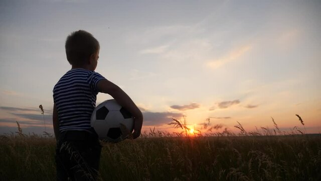 Childhood dream. boy holding soccer ball walking in the park silhouette. happy family kid dream concept. kid boy walking on the field silhouette at sunset carries a fun soccer ball. baby winner