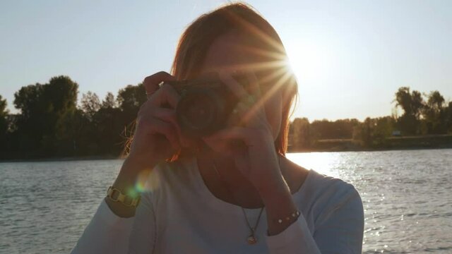 [4k] beautiful ginger woman taking photos with vintage slr camera in front of sun star and backlight at river