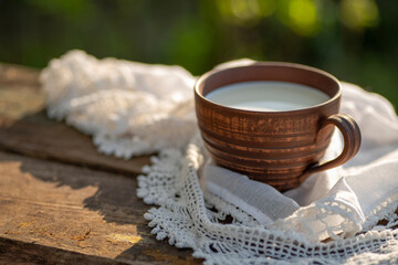 Pottery cup with milk (kefir, yogurt, sour cream, kumis), lace tablecloth, wooden table. Outdoor...