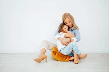 Happy family mom and daughter playing at home. Family sitting on floor and playing and hugging, showing different grimaces together and laughing at it. 