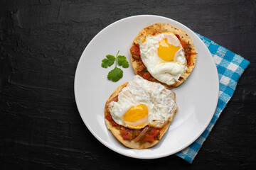 Fried eggs with sauce and tortilla called rancheros for  breakfast on dark background. Mexican food
