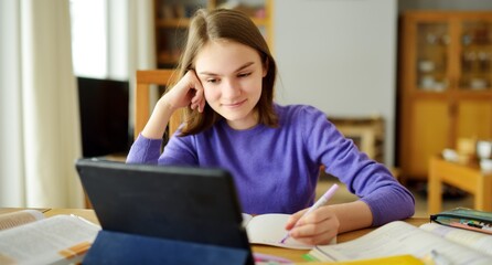 Preteen schoolgirl doing her homework with digital tablet at home. Child using gadgets to study. Education and distance learning for kids. Homeschooling during quarantine.
