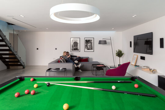 Couple relaxing in their modern apartment with pool table in foreground.