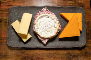 A slate trey of three different types of cheese's on a wooden background