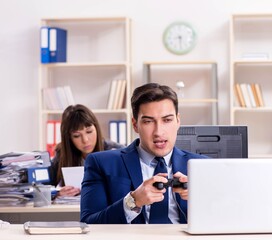 Man playing games in office while colleague is busy
