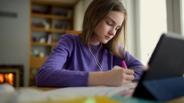 Preteen schoolgirl doing her homework with digital tablet at home. Child using gadgets to study. Education and distance learning for kids. Homeschooling during quarantine. Stay at home entertainment.