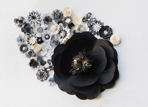 Big black flower with smaller paper flowers on white wall