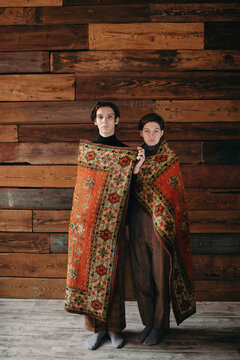 Young models wrapping in carpet and posing on wooden background