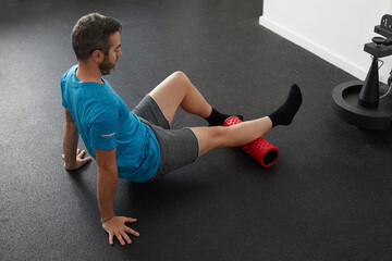 Male exercising the leg muscles with a roller foam in a fitness club