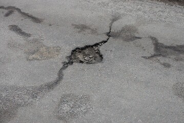 one pothole from a hole with a crack on the gray asphalt road on the street
