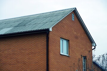 facade of a brown brick private house with windows under a gray slate roof against the sky