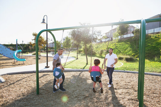 Two dads playing with their kids at the playground on sunny day
