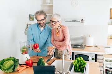 Senior couple preparing healthy smoothie in kitchen and using tablet to read recipe
