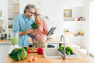 Senior couple preparing healthy smoothie in kitchen and using tablet to read recipe